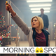Jodie Whittaker's 13th Doctor holds her Sonic Screwdriver aloft as she explores a warehouse decorated with Christmas lights.